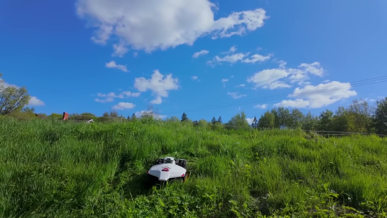 Robotic mower on a steep meadow bank under a blue sky